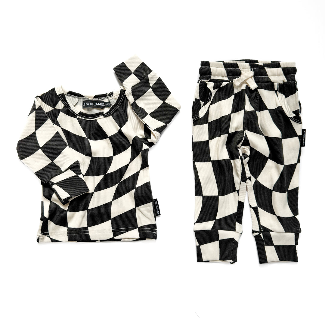 A children's two-piece outfit set featuring a long-sleeve top and matching pants in a black and off-white checkerboard pattern, laid flat on a white background.