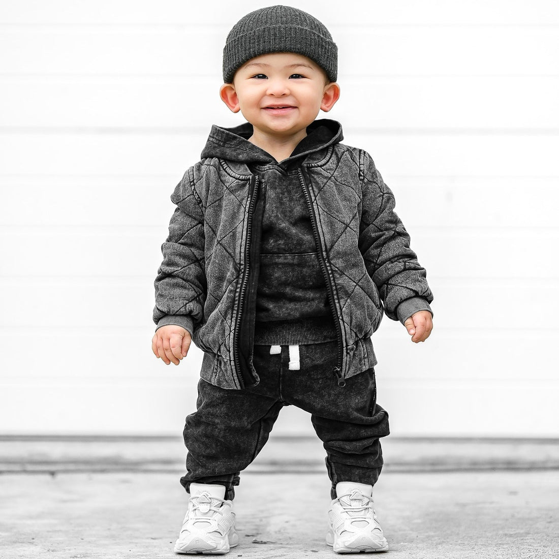 Toddler boy wearing LENOX JAMES charcoal acid wash joggers with a matching black washed hoodie, gray quilted bomber jacket, charcoal knit beanie and white sneakers for a cool layered kids&
