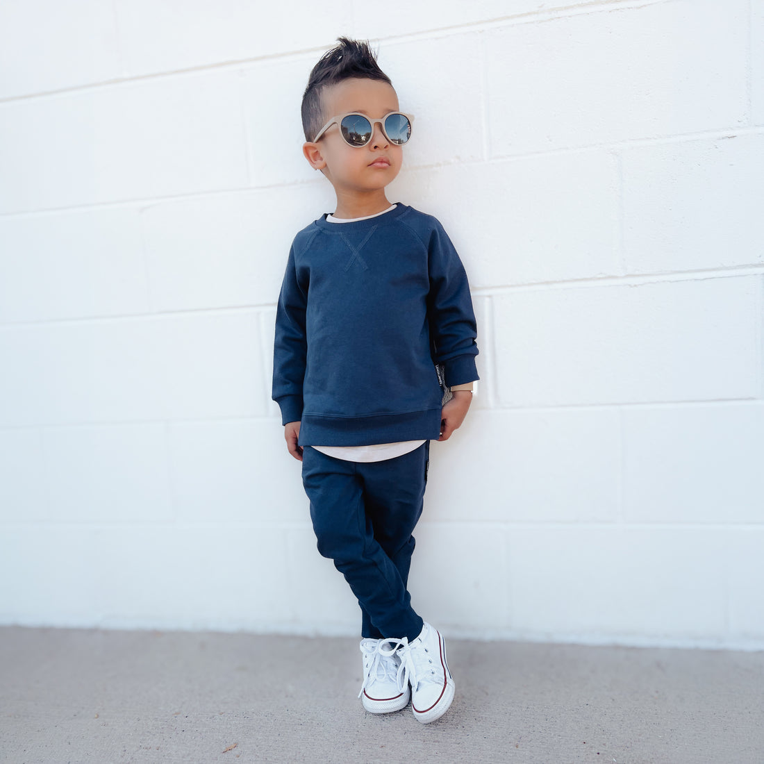 Toddler boy wearing LENOX JAMES midnight navy joggers with a matching navy crewneck sweatshirt, sunglasses and white sneakers, styled as a casual kids&