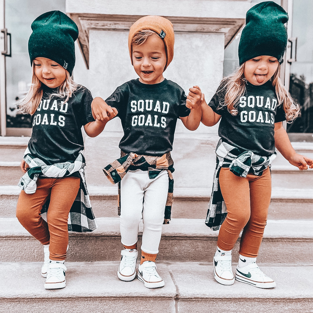 Three children wearing matching 'Squad Goals' shirts on a staircase.